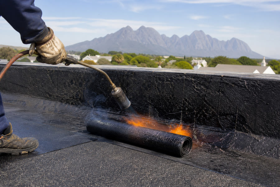 Torch-on bitumen membrane being applied to a flat roof, Helderberg in the distance.